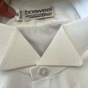 Vit skjorta från Bosweel - Klassisk vit skjorta från Bosweel i 100% bomull. Skjortan har en stilren design med lång ärm, klassisk krage och knäppning framtill. Perfekt för dig som vill ha en enkel och tidlös look. Ny ouppackad 