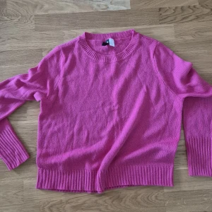 Rosa stickad tröja från H&M - Säljer en snygg rosa stickad tröja från H&M med rund hals och långa ärmar. Tröjan har breda ribbade muddar vid ärmslut och nederkant, perfekt för dig som gillar färg och vill ha en enkel men trendig look.