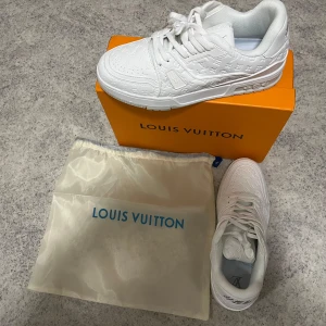 Vita Louis Vuitton sneakers i skinn - Exklusiva helvita Louis Vuitton sneakers i skinn med präglat LV-monogram över hela skon. Klassisk rund tå, snörning och platt sula. Snygg och clean design med diskreta logodetaljer på plös och sula. Kommer med originalkartong och dustbag.
