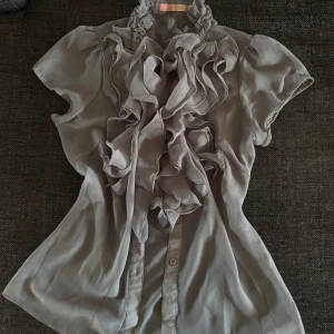 Grå volangblus  - Supersnygg grå blus från Saint Tropez med korta ärmar och massor av volanger framtill. 