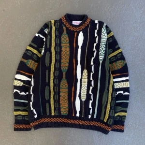 Mönstrad stickad tröja från Campus XL - Fet stickad tröja från Campus i storlek XL med unikt mönster i svart, grön, orange, vit och oliv. Tröjan har ribbade muddar och krage, och är tillverkad i 100% bomull. Perfekt för dig som gillar retrovibbar och färg.