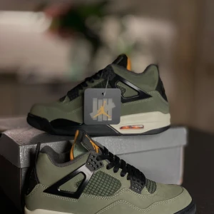 Nike Air Jordan 4 Undefeated Olive - Nike Air Jordan 4 Undefeated i olivgrönt skinn med svarta och orange detaljer. Klassisk siluett med svart snörning, meshpaneler och orange Jumpman-logga på plösen. Grå och orange insida, svart yttersula med orange Nike-detalj. Perfekt för dig som vill sticka ut.