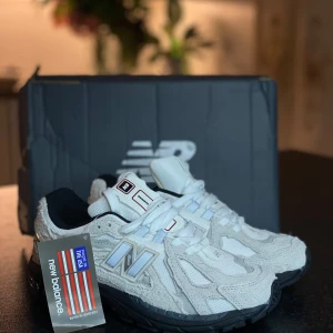 New Balance 1906R vita sneakers - Snygga New Balance 1906R sneakers i vitt med svarta detaljer och robust svart sula. Ovandelen är i mesh och mocka med reflekterande silverdetaljer och klassisk N-logga på sidan. Skorna har snörning och en sportig vibe, perfekta för dig som gillar streetwear.