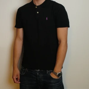 Svart pikétröja från Ralph Lauren - Svart pikétröja från Polo Ralph Lauren i klassisk passform. Tröjan har korta ärmar, krage och två knappar framtill. Perfekt till skolstart. Pris kan diskuteras