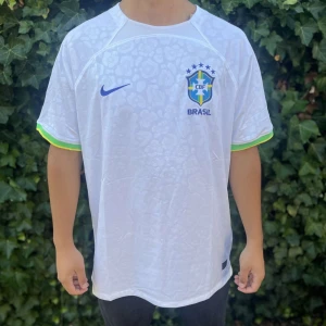 Vit Brasilien fotbollströja Nike - Säljer en vit Brasilien fotbollströja från Nike med diskret leopardmönster, blå Nike-logga och Brasilien-emblem på bröstet. Tröjan har korta ärmar med gröna och gula detaljer vid ärmslut. Perfekt för dig som älskar fotboll och vill representera Brasilien. 																																																																																																												              		Nypris:850kr GORILLAPRIS:365kr                     Skick:10/10 med tagg                               KVITTO MEDKOMMER!