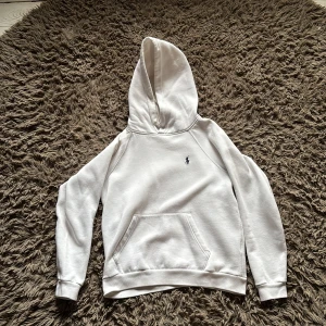 Vit hoodie från Polo Ralph Lauren - Säljer en stilren vit hoodie från Polo Ralph Lauren med klassisk broderad logga på bröstet. Tröjan har huva, magficka och långa ärmar. Perfekt för dig som gillar en clean och enkel look. Materialet är mjukt och skönt, troligtvis bomull.