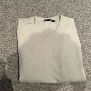 Beige och svart stickad tröja J.Lindeberg - Två stilrena stickade tröjor från J.Lindeberg i beige och svart. Båda har rund hals och diskret logga broderad på bröstet. Perfekt för dig som gillar enkel och clean design. Passar dig som vill ha en klassisk look med snygga färger.