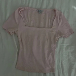Ljusrosa ribbad topp från Amisu, newyorker - Supersöt ljusrosa topp från Amisu, new yorker med fyrkantig urringning och korta ärmar. Ribbad struktur som ger en snygg passform och lite stretch. Perfekt att styla med jeans eller kjol för en trendig look.