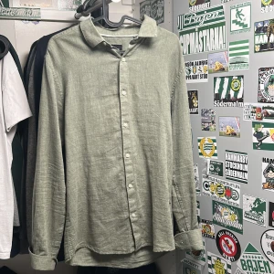 Olivgrön linneskjorta Only & Sons - Snygg olivgrön skjorta från Only & Sons i linnematerial. Skjortan har klassisk krage, vita knappar och lång ärm. Slim fit-modell som ger en clean och modern look. Perfekt för dig som gillar stilrena plagg med avslappnad känsla. Storlek S