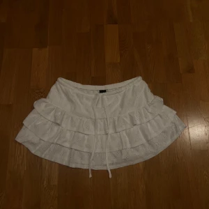 Vit volangkjol med broderi från Gina Tricot - Superfin vit kortkjol från Gina Tricot med broderade detaljer och flera volanger. Kjolen har snörning i midjan och är gjord i bomull, perfekt för en fräsch och somrig look. Säljer pga felköp, lappar kvar!