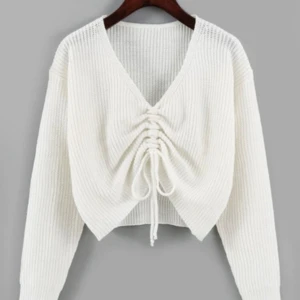 Vit stickad kofta med snörning - Säljer en vit stickad tröja med v-ringad hals och snygg snörning framtill som ger en croppad look. Tröjan har långa ärmar och ribbade muddar. 