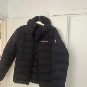 Svart dunjacka Peak Performance - Svart dunjacka från Peak Performance med huva och diskret logga på bröstet. Endast seriösa köpare.