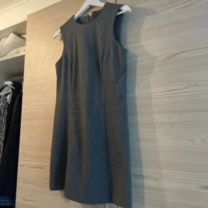 Grå ärmlös kortklänning - Snygg grå klänning med enkel och stilren design. Modellen är ärmlös med rund halsringning och har en rak passform. Klänningen är kort och har en diskret dragkedja i ryggen. Använd endast 1 gång!