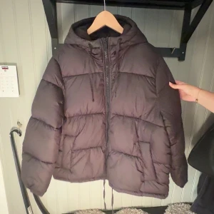 Svart pufferjacka från H&M med huva - Säljer en svart pufferjacka från H&M i storlek S. Jackan har en stor huva, dragkedja framtill. Den är vadderad och har en oversized look, perfekt för kalla dagar. Enkel och stilren design som funkar till det mesta.