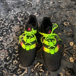 Adidas fotbollsskor svart/neongul/rosa - Säljer ett par Adidas fotbollsskor i storlek 46 med snygg design i svart, neongult och rosa. Skorna har snörning, mönstrad ovandel och dobbar för bra grepp på planen. Perfekta för dig som vill sticka ut på matchen!