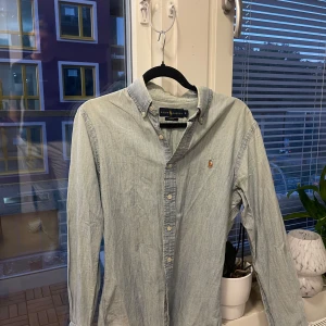 Ljusblå jeansskjorta från Ralph Lauren - Säljer en stilren jeansskjorta i ljusblått från Ralph Lauren i slim fit-modell. Skjortan har klassisk krage, knappar hela vägen och den ikoniska broderade loggan på bröstet. Storlek S