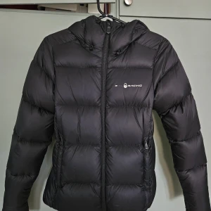 Svart dunjacka Sail Racing XS - Säljer en svart dunjacka från Sail Racing i storlek XS. Jackan har huva, dragkedja framtill och två sidofickor med dragkedja. Puffig modell med diskret logga på bröstet och tryck på huvan. Yttertyg i nylon och fyllning av ankdun och fjäder.