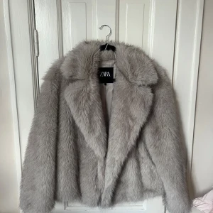 Grå pälsjacka från Zara - Supermjuk och fluffig grå pälsjacka från Zara med bred krage och lång ärm. Jackan har en oversized känsla och är perfekt för att ge din outfit en lyxig vibe. Fodrad insida för extra komfort och värme. Snygg att styla till både jeans och klänning.