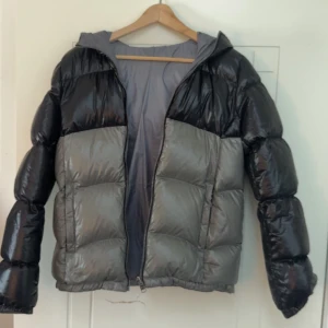Svart och grå pufferjacka med huva - Säljer en riktigt fet pufferjacka från Colmar i svart och grått. Jackan har en schysst glansig finish. Perfekt för dig som vill sticka ut och hålla dig varm under vintern. Dragkedja framtill och logga på armen!