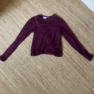 Mörklila långärmad topp från Gina Tricot - Snygg mörklila långärmad topp från Gina Tricot med spetsdetaljer vid v-ringad hals. Mjuk och skön i bomullsmaterial.  Andvänd mycket men är i bra skick!
