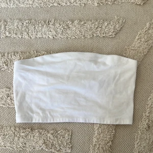 Vit bandeau tubtopp - Enkel och stilren vit bandeau tubtopp från 157 i storlek XS/S. Toppen är ärmlös och axelbandslös, perfekt för varma dagar eller lager på lager. Gjord i mjuk bomull som sitter skönt mot huden. 