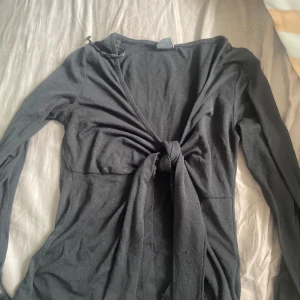 Svart omlotttröja Gina Tricot XS - Supersnygg svart tröja från Gina Tricot i storlek XS. tröjan har lång ärm, omlott-design med knyt framtill och en djup v-ringning. Mjuk och stretchig bomull som sitter skönt och ger en slim passform. Perfekt för dig som gillar stilrena och trendiga plagg.