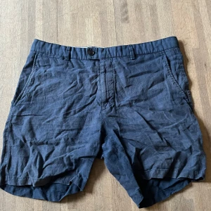 Mörkblå linneshorts från Tiger Of Sweden - Snygga mörkblå shorts i linne med klassisk passform. De har två sidofickor fram och två bakfickor, samt hällor för bälte. Perfekta för varma dagar och en chill stil.