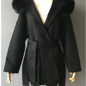 Svart kappa med fuskpäls och bälte - Stilren svart kappa med breda ärmar, stor huva med fluffig fuskpäls och knytbälte i midjan. Perfekt för dig som vill ha en klassisk look med en twist. Kappan har omlottstängning och ger en snygg siluett.