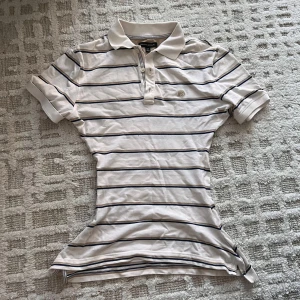 Vit randig pikétröja Banana Republic - Vit pikétröja från Banana Republic med svarta och grå tunna ränder. Klassisk krage, korta ärmar och knappar vid halsen. Perfekt för en clean och sportig stil. Skön bomullskvalitet och normal passform.