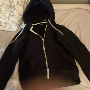 Svart hoodie Sweet Pants med dragkedja - Svart hoodie från Sweet Pants i storlek 12y med vit broderad logga på huvan och patch på ärmen. Tröjan har hel dragkedja, huva med snörning. Den har ett väldigt litet hål på vänster armen men det syns knappt den är även lite solblekt men super fin tröja ändå. Köpt för 1100 i Frankrike säljer för 400