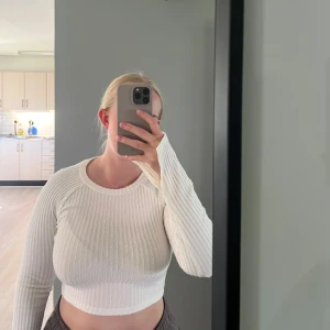 Vit ribbad långärmad croptop - Säljer en vit ribbad långärmad croptop med rund halsringning. Tröjan är figurnära och har stretchigt material. Har slits vid ärmarna 