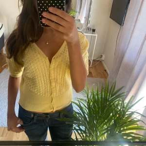 Gul stickad kofta med v-ringning - Söt ljusgul stickad kofta med v-ringning och korta ärmar. Koftan har fina stickade detaljer, ribbad nederkant och knäpps med små knappar framtill. 