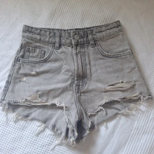 Gråa jeansshorts från Zara - Snygga gråa jeansshorts från Zara med slitna detaljer och fransig kant. Klassisk femficksmodell och råa kanter för en cool vibe. Perfekta för sommaren och lätta att matcha med allt.