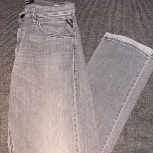 Replay THAD Jeans - Snygga grå jeans från Replay med klassisk femficksdesign och raka ben. Jeansen har en ljusgrå tvätt, svarta detaljer och tydlig Replay-logga på fickan. Perfekta för dig som gillar en stilren och avslappnad look.