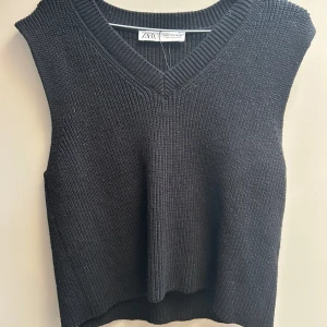 Svart stickad väst från Zara - En svart stickad väst från Zara med v-ringad hals och ribbade kanter. Västen har en klassisk, enkel design och är perfekt att styla över en skjorta eller t-shirt för en trendig lager-på-lager-look.