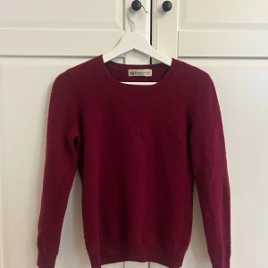 Vinröd stickad tröja från Shanjian - Vinröd stickad tröja från Shanjian med rund halsringning och långa ärmar. Tröjan har ribbade muddar vid ärmslut och nederkant, perfekt för lager på lager under kyliga dagar. Enkel och stilren design som funkar till det mesta.