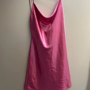 Rosa satin slipklänning - Snygg rosa slipklänning i glansigt satinmaterial med tunna axelband och avslappnad passform. Klänningen har en draperad urringning och är perfekt för dig som vill sticka ut med en färgstark look.