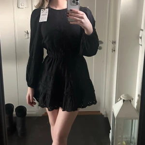 Svart broderad kortklänning från Zara - Supersöt svart kortklänning från Zara med broderade detaljer och volangkant. Klänningen har lång ärm, markerad midja med resår och rund halsringning. Perfekt för dig som gillar romantisk och trendig stil💗