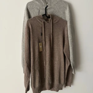 Kashmirhoodie i beige och grå - Två helt nya hoodies i 100% kashmir, en i beige och en i ljusgrå. Båda har huva, snörning och långa ärmar. Mjuka och lyxiga med ribbade muddar vid ärmslut och nederkant. Perfekt för dig som vill ha en chill och stilren look.