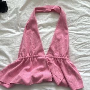Rosa ribbad halterneck topp - Supersöt rosa halterneck topp med djup v-ringning och volangliknande nederdel. Toppen är ribbad och har en bred krage i nacken. Perfekt för dig som vill sticka ut med en feminin och trendig look.