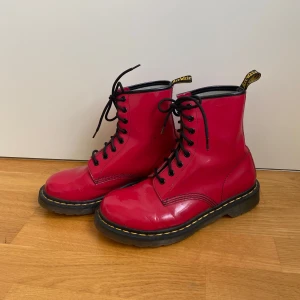 Röda Dr. Martens boots  - Säljer ett par röda Dr. Martens boots med klassisk gul söm och svart snörning. Har inte använts mycket så dem är fortfarande formbara, men har fått några smärre defekter vid fest! 