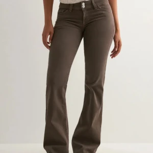 Bruna bootcut jeans med hög midja - Snygga bruna jeans med bootcut-modell och hög midja. Byxorna har klassiska fem fickor och coola detaljer på bakfickorna. Perfekta för dig som vill ha en trendig och bekväm look. Materialet är mjukt och stretchigt för extra komfort.