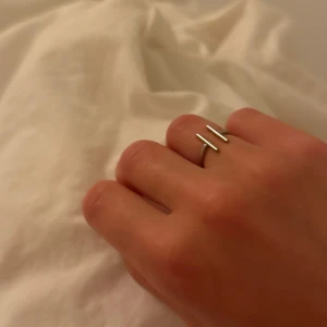 Minimalistisk ring - Säljer en stilren och modern ring i silverfärg med två raka stavar framtill. Ringen har en öppen design som ger en cool och trendig känsla. Perfekt för dig som gillar minimalistiska smycken och vill ha något som sticker ut lite extra. Går att justera storleken. 