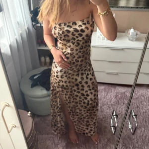 Leopardmönstrad långklänning från Zara - Säljer en snygg långklänning från Zara med leopardmönster. Klänningen har tunna axelband, öppen rygg och en hög slits framtill. Materialet är glansigt och känns lyxigt mot huden. Perfekt för dig som vill sticka ut och känna dig extra glam. Endast testad!