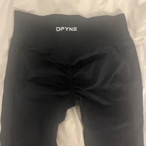Svarta leggings från DFYNE - Svarta leggings från DFYNE med hög midja och tight passform. Tillverkade i ett stretchigt syntetmaterial som sitter skönt och följer kroppen. Perfekta för träning eller chill. Diskret logga framtill i vitt.