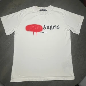 Palm Angels vit t-shirt Tokyo print - Palm Angels t-shirt i vit bomull med korta ärmar och rund hals. Framsidan har ett stort svart Tokyo-print och Palm Angels-logga med röd spray-effekt över. Snygg streetwear vibe och klassisk passform. Perfekt för dig som gillar statement-plagg.                          ‼️KOLLA SISTA BILDEN‼️ Går säkert bort med något speciellt tvättmedel, men aldrig testat🙂