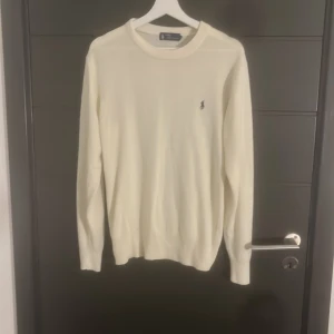 Vit/ beige stickad tröja från Ralph Lauren - Säljer en snygg vit/beige stickad tröja från Ralph Lauren med klassisk rund hals och diskret logga broderad på bröstet. Långärmad och mjuk i materialet, perfekt för dig som gillar stilrena och enkla plagg. Passar dig som vill ha en clean look. Tröjan passar storlek S samt M
