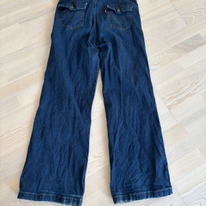 Levi's 512 wide jeans med ficklock - Mörkblå jeans från Levi's med breda ben och snygga ficklock bak med knappdetaljer. Klassisk denim med slitna kanter nertill och kontrastsömmar. Mina absoluta favoriter som tyvärr inte passar längre. . Stl M 14 men är väldigt rymliga så jag säger snarare Large/XL. 