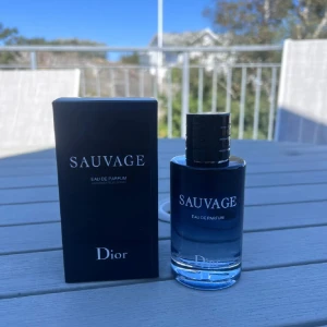 Dior Sauvage Eau de Parfum - Dior Sauvage Eau de Parfum med elegant mörkblå glasflaska och svart lock. Flaskan har en stilren, rund form och tydlig vit text. Parfymen kommer i originalkartong med samma mörka, lyxiga design. En ikonisk doft för dig som vill sticka ut.