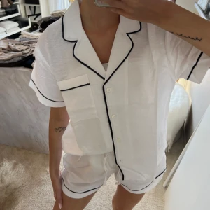 Vita linne pyjamas från H&M - Snygg vit linne pyjamas från H&M med svarta kontrastkanter. Luftigt material i bomull och linne, perfekt för chill dagar hemma eller när du vill ha det extra bekvämt. Klassisk look med loose passform och stilrena detaljer.